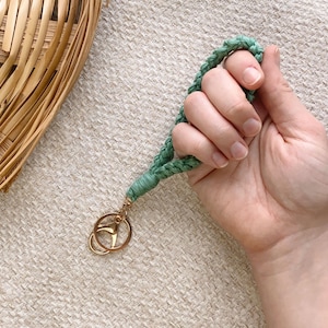 May include: A green braided keychain with a gold key ring. The keychain is made of a soft, woven material.