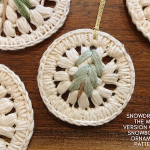 Puede incluir: Primer plano de un adorno de crochet blanco con un dise&ntilde;o bordado en verde y marr&oacute;n. El adorno est&aacute; colgado de una cuerda dorada. El texto "SNOWDROP IS THE MINI VERSION OF THE SNOWBOUND ORNAMENT PATTERN" est&aacute; escrito debajo del adorno.