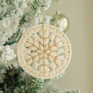 Puede incluir: Un adorno de copo de nieve de crochet blanco colgado de un &aacute;rbol de Navidad nevado.