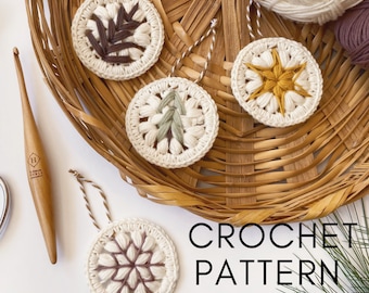 May include: Four crocheted ornaments in a wicker basket. The ornaments are white with different colored accents: brown, yellow, green, and purple. The ornaments are decorated with a leaf, a star, a tree, and a snowflake. The text "CROCHET PATTERN" is visible below the basket.