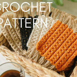 May include: A basket filled with crocheted coasters in various colors, including orange, beige, black, and white. The coasters have fringe edges and are made with a textured stitch.