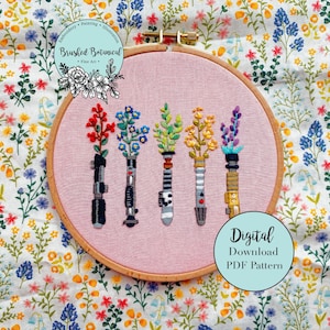 May include: Five embroidered light sabers with floral designs in a pink embroidery hoop. The floral designs are red, blue, green, yellow, and purple. The hoop is on a white background with a floral pattern.
