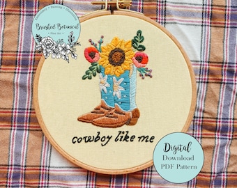以下が含まれることがあります： 青いカウボーイブーツにひまわりと他の花が飾られた刺繍のフープアート。ブーツの下には「cowboy like me」という文字が刺繍されています。フープは格子縞の布地に置かれています。デジタルダウンロードPDFパターンです。