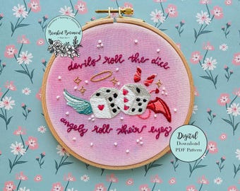 以下が含まれることがあります： ピンクの刺繍枠に、翼のついたサイコロ2つと「devils roll the dice angels roll their eyes?」というテキストのデザインが施されています。デジタルダウンロードPDFパターン