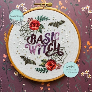 Könnte beinhalten: Stickerei auf einem Stickrahmen mit dem Text "Basic Witch" in lila und schwarzer Schrift. Der Rahmen ist mit einem Spinnennetz, Fledermäusen und roten Rosen verziert.