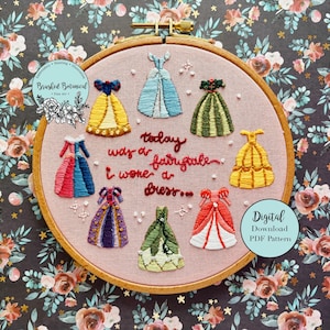 May include: Embroidered hoop art with a pink background featuring seven colorful princess dresses and the text "Today was a fairytale, I wore a dress".