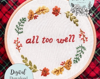 以下が含まれることがあります： 秋葉とベリーのリースが「all too well」というテキストを囲む、刺繍のフープアート。フープは赤と黒の格子縞の布の上に置かれています。