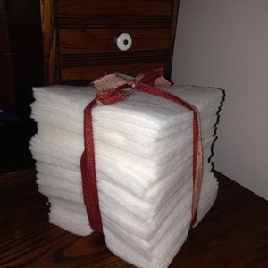 May include: A stack of white fabric squares tied together with a red and white ribbon. The fabric squares are arranged in a rectangular shape.