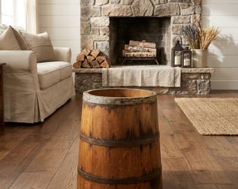 Peut inclure: Un tonneau cylindrique en bois avec une finition brun clair naturelle et un grain de bois visible, renforcé par deux bandes métalliques sombres entourant l'extérieur et un bord métallique sur le dessus, posé sur un sol en bois.
