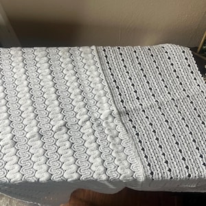 May include: A white, textured, knitted blanket with a detailed pattern. The blanket is divided into two sections, one with a wavy design and the other with a dotted pattern. The blanket is made of a soft material and is suitable for home decor.