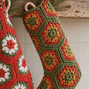 Peut inclure: Deux chaussettes de Noël composées de carrés granny crochetés. L'une présente une base rouge avec des motifs floraux blancs et verts, tandis que l'autre a une base verte avec des motifs floraux rouges et jaunes. Elles sont suspendues.