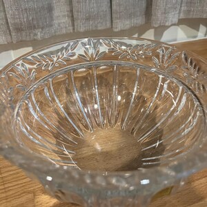 May include: A clear glass bowl with a decorative leaf pattern around the rim. The bowl has vertical ridges on the inside and sits on a wooden surface. The glass is transparent, allowing light to pass through.