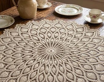 May include: A round, cream-colored crochet doily featuring an intricate, radiating peacock feather pattern. The textile displays a dense, symmetrical design with a central circular motif that expands into repeating leaf-like shapes toward the scalloped edge.