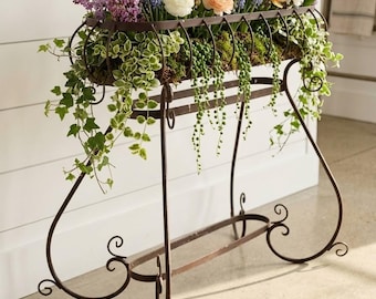 Peut inclure: Un support pour plantes en métal brun foncé avec un panier rectangulaire rempli de fleurs colorées, notamment des roses, jaunes et blanches, des brins de lilas violets et des plantes retombantes comme du lierre et du séneçon.