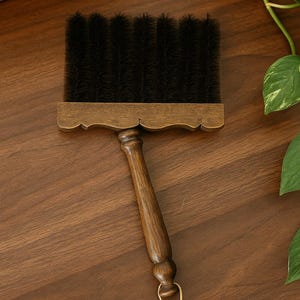 May include: A wooden brush with a dark bristle head and a long, curved handle. The brush has a decorative, scalloped edge where the bristles meet the handle. A small loop is attached to the end of the handle.