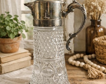 Peut inclure: Une carafe vintage en verre transparent avec un couvercle et une poignée en métal argenté. La carafe présente un motif taillé en diamant et une poignée décorative. Une pièce classique pour servir des boissons, ajoutant de l'élégance à toute table.