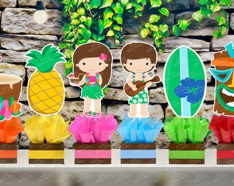 May include: Six luau themed centerpieces with a brown base and colorful tissue paper. The centerpieces feature a pineapple, a coconut, a surfboard, a tiki mask, and two figures wearing leis.