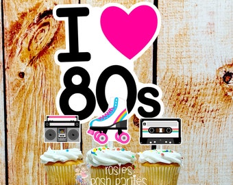 May include: A three-tier cupcake stand with cupcakes decorated with 80s themed toppers. The toppers include a boombox, roller skates, a cassette tape, a Rubik's cube, a Game Boy, and a heart with the text "I love 80s".