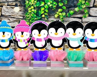 May include: Six penguin centerpieces with different colored hats and scarves. Each penguin is sitting on a small white box with tissue paper in blue, pink, purple, and green.