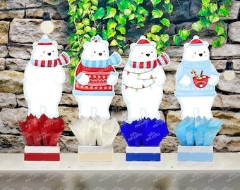 May include: Four polar bear cutouts with festive sweaters, hats, and scarves, each atop a decorative box with tissue paper. The bears have different designs, including a sweater with Christmas lights and one holding a mug of hot cocoa. The boxes are red, white, blue, and light blue.