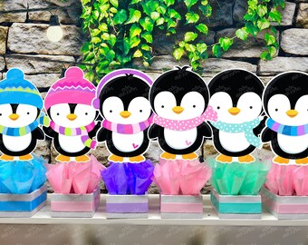 May include: Six penguin centerpieces with different colored hats and scarves. Each penguin is standing on a small box with tissue paper inside. The boxes are blue, pink, purple, pink, green, and pink.