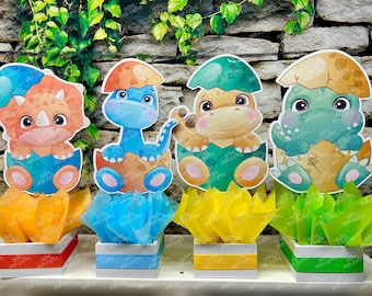 May include: Four colourful dinosaur centrepieces with tissue paper flowers. Each centrepiece features a different dinosaur in a nest with a blue, green, orange, or yellow base.