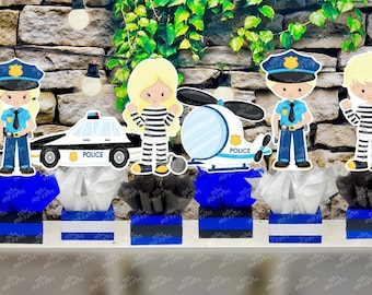 May include: Five centerpieces for a police-themed party. Each centerpiece features a different character: a police officer, a police officer, a prisoner, a police car, and a police helicopter. The centerpieces are decorated with blue and white tissue paper and blue and white ribbon.