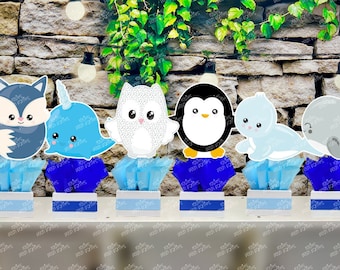 May include: Six blue and white centerpieces with animal characters. The characters are a fox, a narwhal, an owl, a penguin, a seal, and a whale. The centerpieces are made of cardboard and are decorated with blue and white paper.