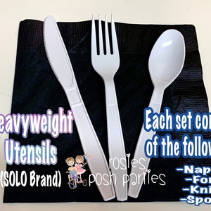 Op de afbeelding: Een set van zware witte plastic bestek op een zwarte servet. De set bevat een vork, mes, lepel en servet. De tekst "Heavyweight Utensils (SOLO Brand)" is zichtbaar in de afbeelding.