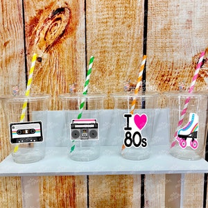 May include: Four clear plastic cups with straws and 80s themed stickers. The stickers feature a cassette tape, a boombox, a heart with the text "I Love 80s", and a pair of roller skates.