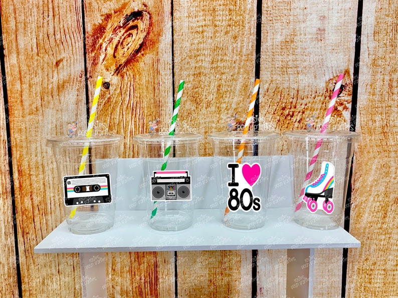 May include: Four clear plastic cups with straws and 80s themed stickers. The stickers feature a cassette tape, a boombox, a heart with the text "I Love 80s", and a pair of roller skates.