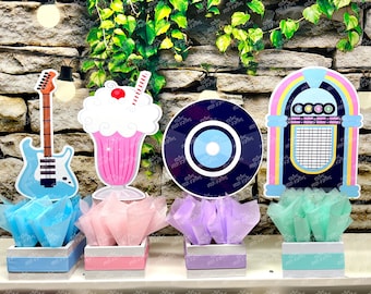 May include: Four centerpieces featuring a blue guitar, a pink milkshake, a black vinyl record, and a blue and pink jukebox. Each centerpiece is placed in a white box with a colored tissue paper base.