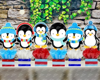 May include: Six penguin centerpieces with blue, red, and white accents. Each penguin is wearing a hat and scarf. The penguins are standing on top of small, round, white, red, and blue bases.