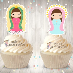 May include: Two cupcakes with white frosting topped with edible images of the Virgin Mary. The images are on white cardstock with a scalloped edge. The cupcakes are on a woodgrain background.