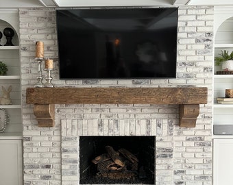 May include: A white brick fireplace with a wooden mantel and a black television above it. The fireplace has a black metal firebox with logs inside.