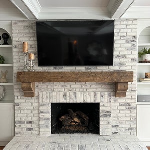 May include: A white brick fireplace with a wooden mantel and a black television above it. The fireplace has a black metal firebox with logs inside.