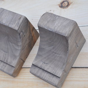 May include: Two wooden corner brackets with a gray stain finish. The brackets are curved on the inside and have a triangular shape.