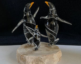 May include: A glass penguin family sculpture with black and white swirl patterns. The penguins are standing on a small, light brown rock base.