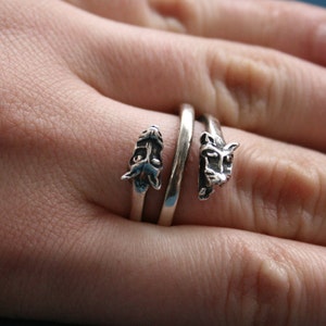May include: A silver ring with two animal heads on it. The ring is wrapped around a finger.