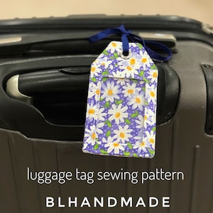 May include: A purple and white daisy patterned luggage tag with a clear plastic window for a name card. The tag is attached to a grey suitcase with a blue ribbon. The text "luggage tag sewing pattern BLHANDMADE" is below the suitcase.
