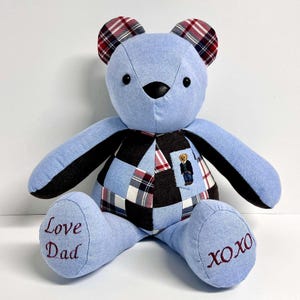 May include: A blue patchwork teddy bear with black and red plaid ears. The bear is wearing a patchwork shirt with a small embroidered bear on the pocket. The bear's paws are embroidered with "Love Dad" and "XOXO".