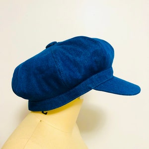 May include: A blue denim newsboy cap with a button on top. The cap has a wide brim and a curved crown.