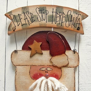 May include: A wooden Santa Claus sign with a banner that reads "Please Stop Here Santa". The sign is painted in a rustic style with a white beard, red hat, and a yellow star.
