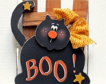 May include: Black wooden Halloween decoration of a cat with a yellow bow and the word "BOO!" in orange letters. The cat has a red nose and black eyes.