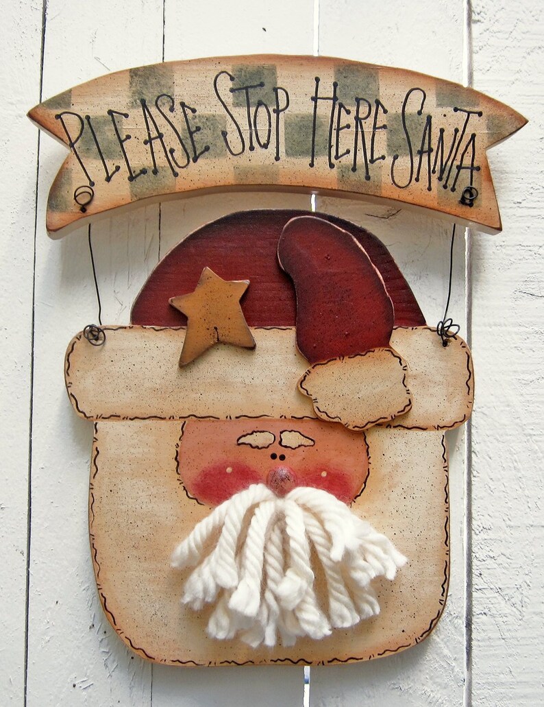 May include: A wooden Santa Claus sign with a banner that reads "Please Stop Here Santa". The sign is painted in a rustic style with a white beard, red hat, and a yellow star.