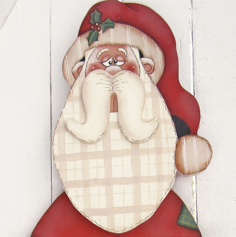 May include: A hand-painted wooden Santa Claus ornament with a red hat, white beard, and plaid pattern. The Santa has a friendly expression and is wearing a red suit with a green plaid trim.