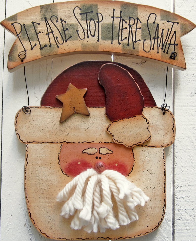 May include: A wooden sign with a painted Santa Claus face and the text "PLEASE STOP HERE SANTA" on a banner above. The Santa Claus face has a red hat, a white beard made of yarn, and a gold star on his hat.