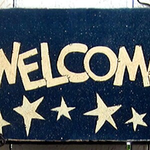 May include: A blue wooden sign with the word "WELCOME" in white lettering. The sign is decorated with five white stars.