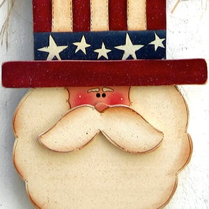 May include: A wooden cutout of a face with a red, white, and blue hat. The hat is decorated with stars and stripes. The face has a white beard and mustache, red cheeks, and black eyes.
