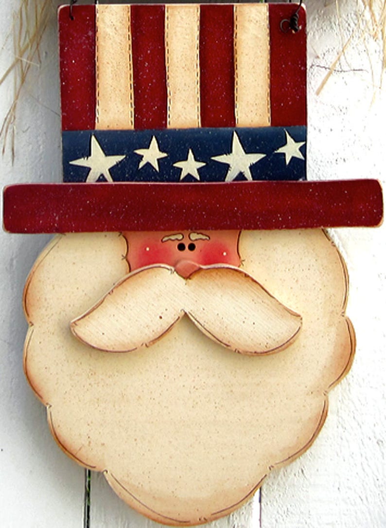 May include: A wooden cutout of a face with a red, white, and blue hat. The hat is decorated with stars and stripes. The face has a white beard and mustache, red cheeks, and black eyes.